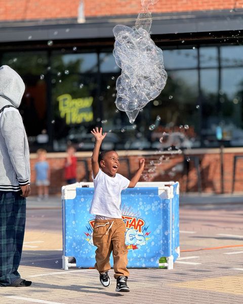 Little boy jumping with arms up and a huge smile beneath a cluster of bubbles