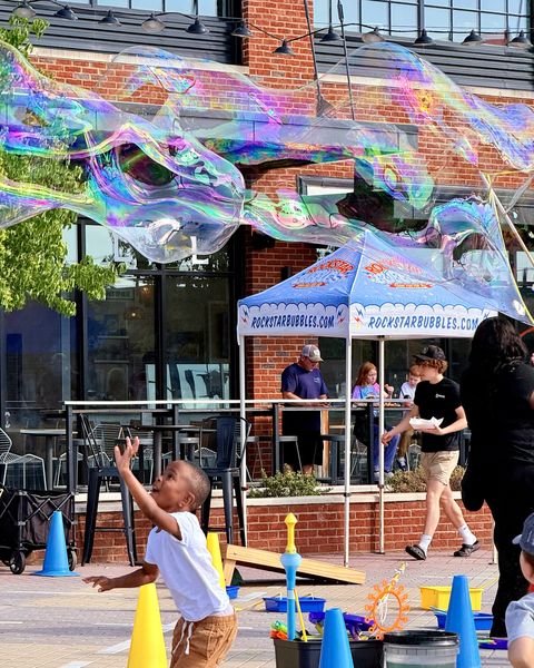 Boy leaping to touch a long, shimmering giant bubble in front of the Rockstar Bubbles tent