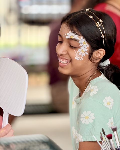 Smiling girl checking her daisy face painting in a hand mirror